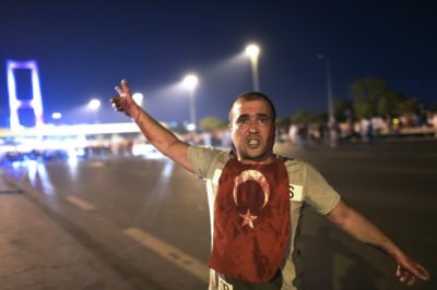 A man covered with blood points at the Bosphorus bridge as Turkish military clashes with people at the entrance to the bridge in Istanbul on July 16, 2016.  Turkish military forces on July 16 opened fire on crowds gathered in Istanbul following a coup attempt, causing casualties, an AFP photographer said. The soldiers opened fire on grounds around the first bridge across the Bosphorus dividing Europe and Asia, said the photographer, who saw wounded people being taken to ambulances.  / AFP PHOTO / Bulent KILIC